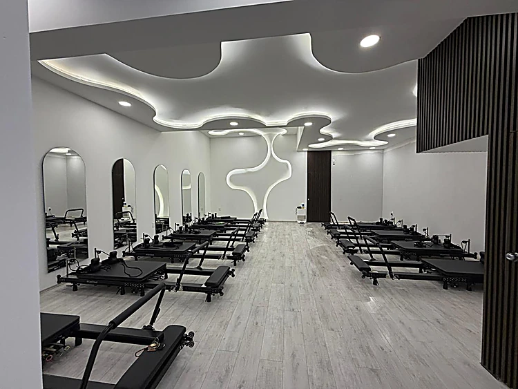 Sala de Reformer de LAJA con el muro blanco esculpido e iluminado, espejos en arco y reformers negros