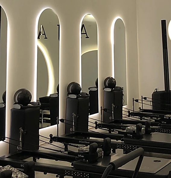Sala de Reformer de LAJA: espejos en arco con luz cálida, letras LAJA reflejadas y reformers negros en fila